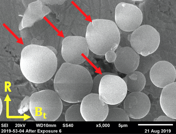 Eroded spherical carbon dust particles after exposure to 30s L-mode plasma in DIII-D divertor. The preferential direction of erosion (red arrow) indicates the direction of the main plasma ions.